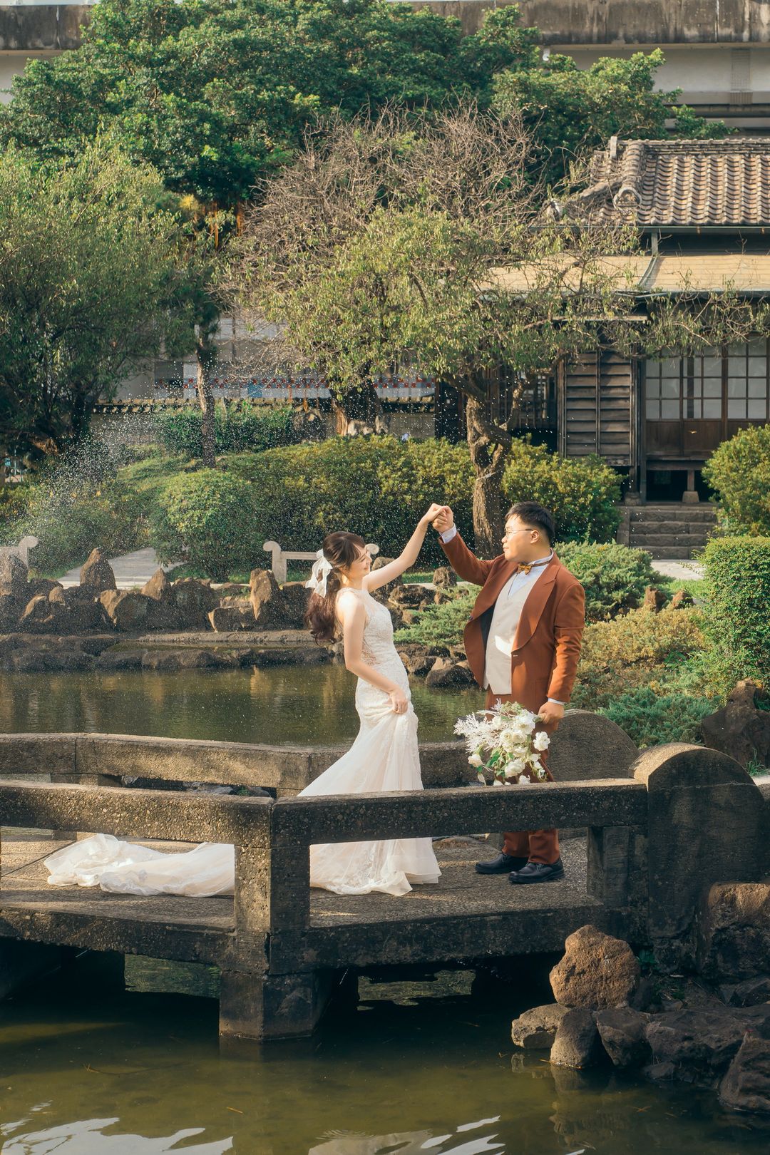 兩人在庭園石橋上牽手轉圈 水花在身後飛揚